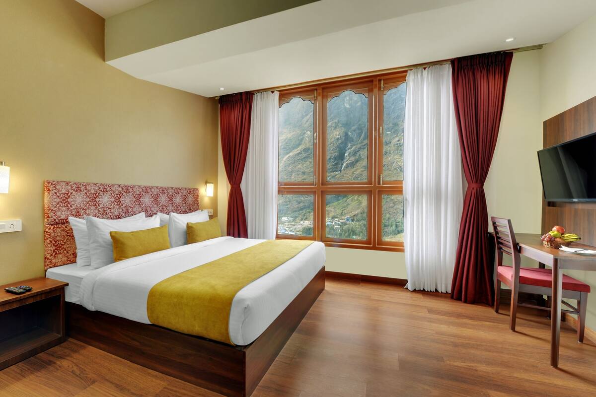 Una habitación de hotel con una cama grande, un escritorio con silla, televisión y una ventana con cortinas.