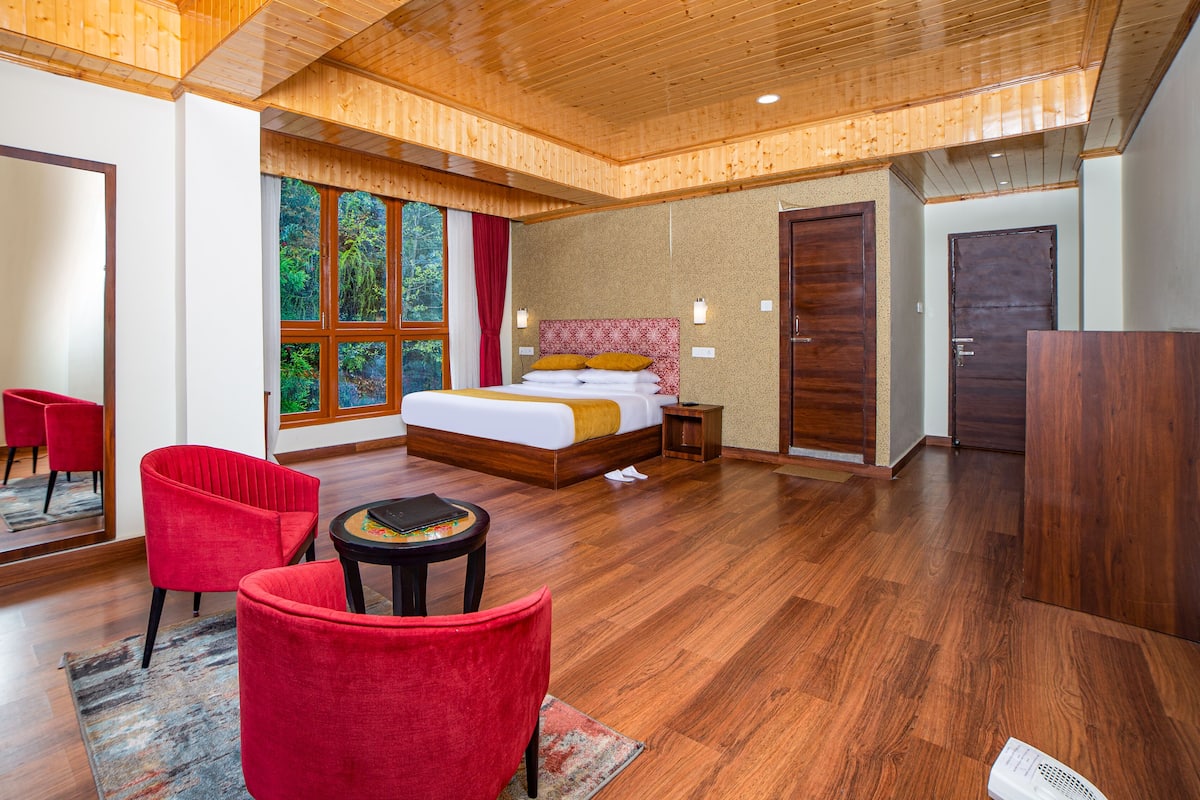Un dormitorio amplio con una cama grande, una zona de estar con un sillón rojo y vistas al exterior a través de un ventanal.