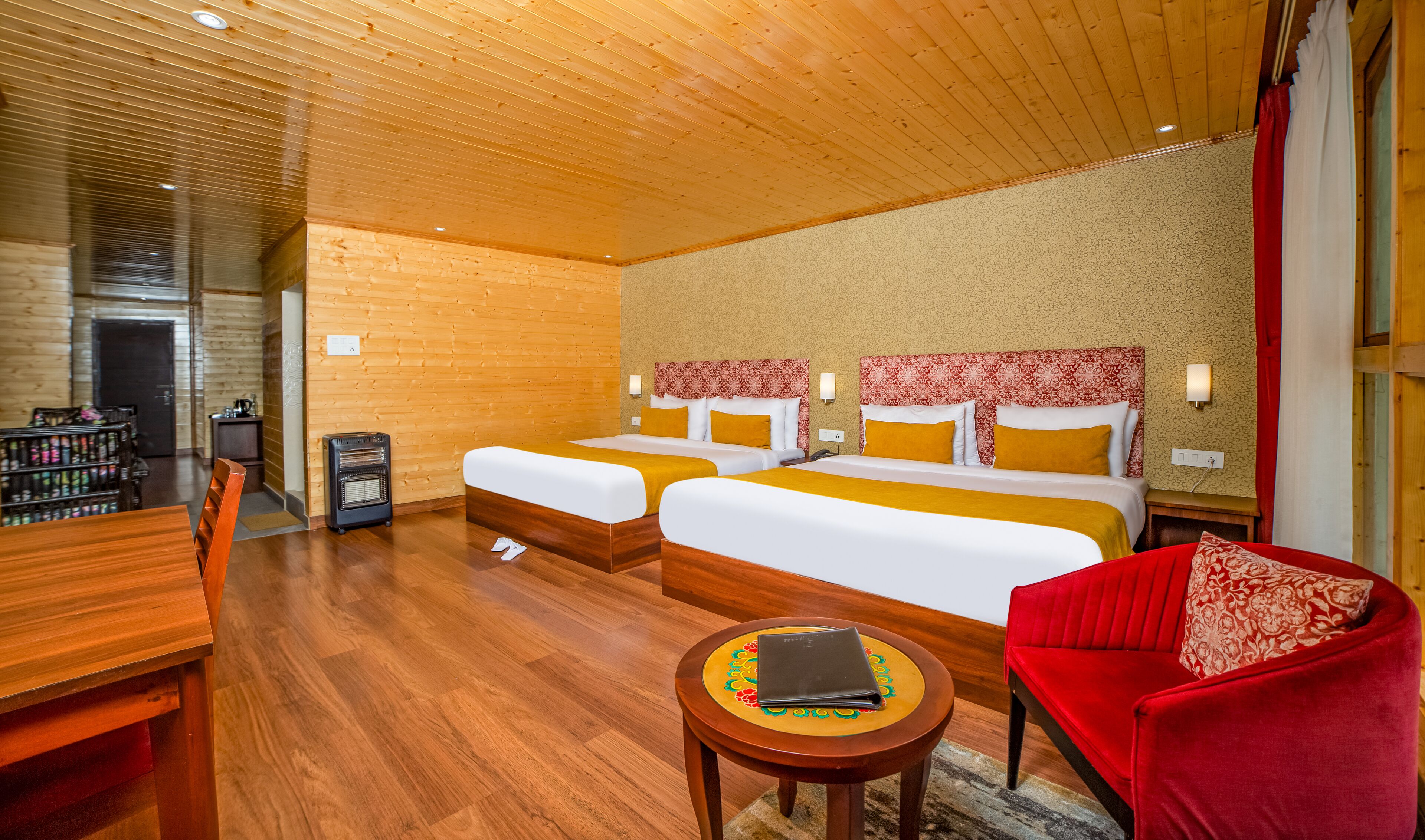 Ein Hotelzimmer mit zwei Betten, einem roten Sessel, einem kleinen Tisch und Holzboden.