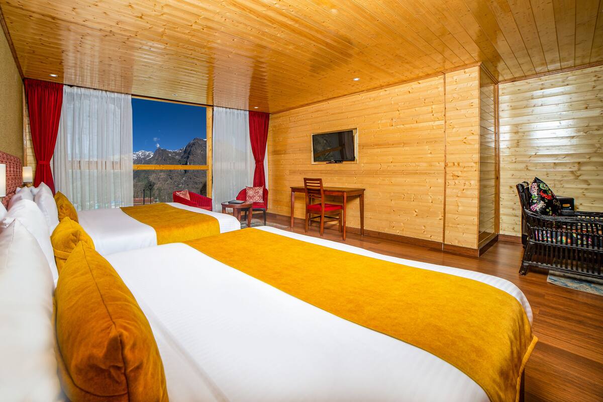 Una habitación de hotel con dos camas, un escritorio, una silla y un televisor en la pared.