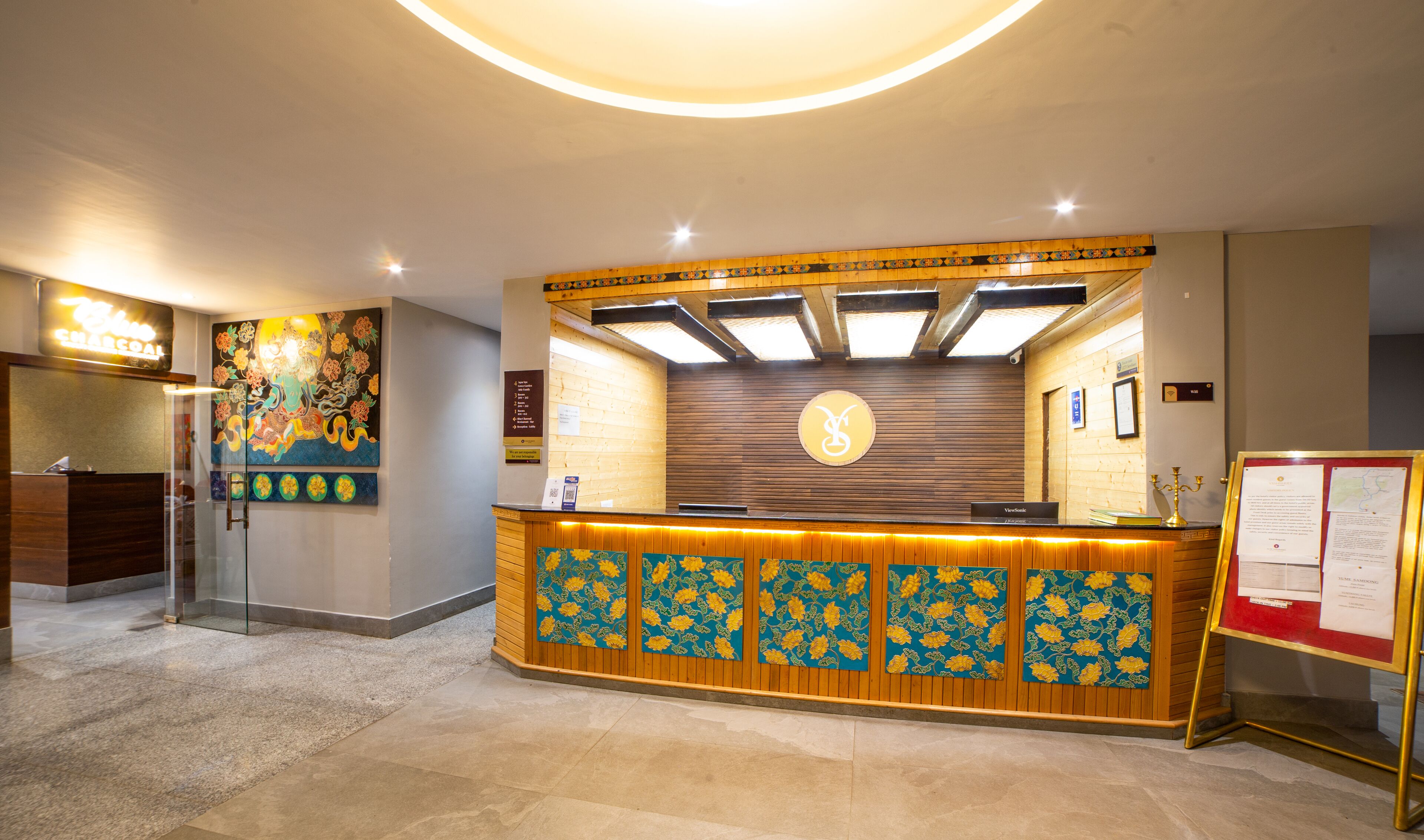 A reception area with a wooden reception desk, a large floral painting on the wall, and a clock above the desk.