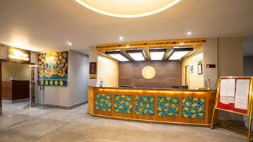 A reception area with a wooden reception desk, a large floral painting on the wall, and a clock above the desk.