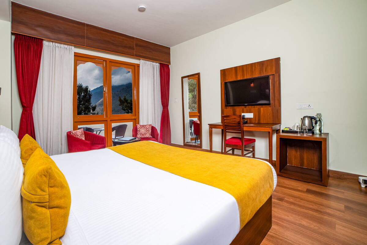 Una habitación de hotel con cama, escritorio, televisor y vista a las montañas desde la ventana.