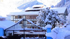 Un chalet tradicional con fachada de madera, un balcón y montañas nevadas al fondo.