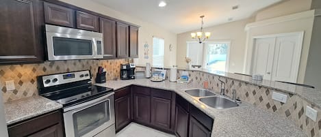 A kitchen with dark wood cabinets, stainless steel appliances, a granite countertop, and a window with blinds.