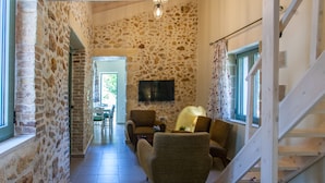 A stone-walled hallway with a staircase, a TV mounted on the wall, and a dining area in the background.