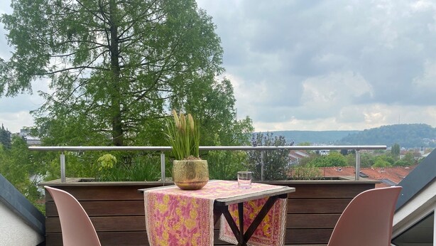 A balcony with a table and two chairs, a potted plant, and a glass of water.