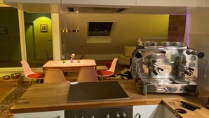 A compact kitchen with a wooden countertop, a coffee machine, and a dining area with chairs and a table.