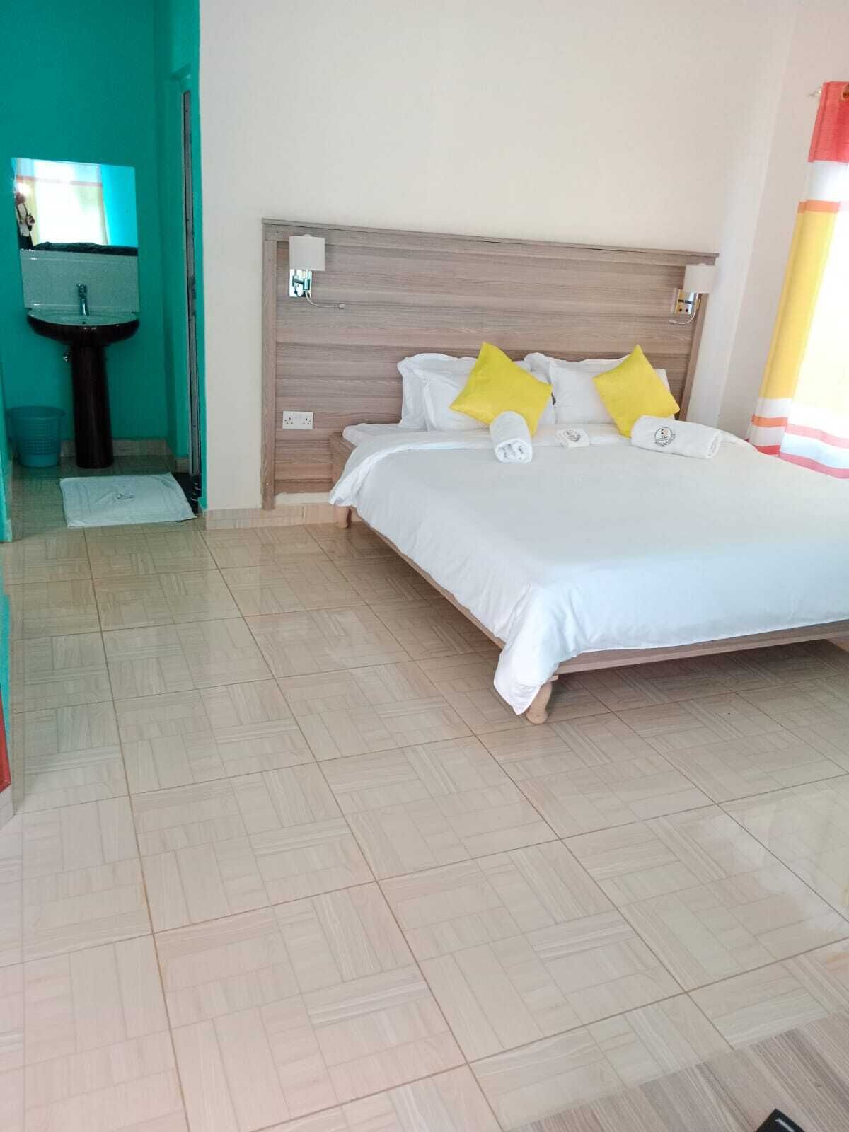 A neatly arranged hotel room with a bed, a wooden headboard, and a small bathroom with a sink and mirror.