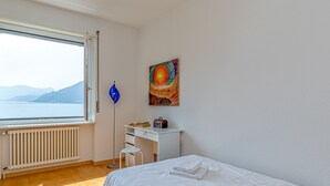 A bedroom with a bed, a desk, a radiator, a window with a view of the sea, and a painting on the wall. - La Luminosa (Bissone)