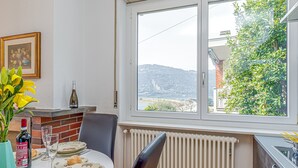 A dining area with a table set for two, a window with a view of hills, a radiator, and a vase with yellow flowers. - La Luminosa (Bissone)
