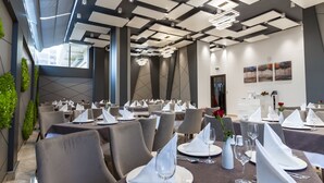 A modern dining area with multiple tables set for service, featuring geometric ceiling designs and ambient lighting. - Hotel Bay Diab (Algiers)