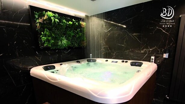 A modern spa area with a hot tub, wooden bench, and a wall-mounted TV. - Hotel Bay Diab (Algiers)