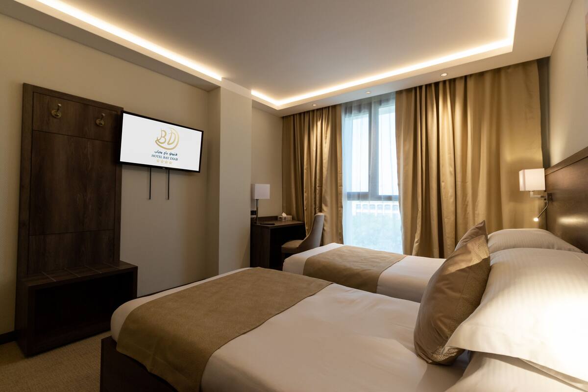 A hotel room with two beds, a desk, a TV, and a view of the city.