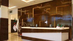 A reception desk with a modern design, featuring a geometric pattern on the wall and a clean, white counter. - Hotel Bay Diab (Algiers)