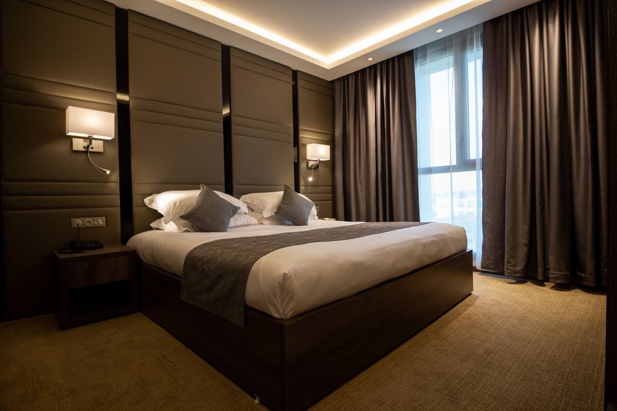 A modern hotel room with a large bed, two bedside tables, and wall-mounted lamps.