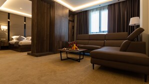 A modern hotel room with a sofa, a small table with fruit, a bed, and a large window with curtains. - Hotel Bay Diab (Algiers)