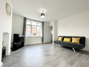 A modern living room with a grey sofa, a flat-screen TV, and a large window with curtains. - Worksop Newly Refurbished 2-bedroom House (Worksop)