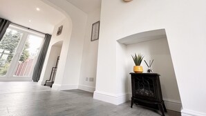 A spacious room with a large window, a clock on the wall, and a small black cabinet with a plant. - Worksop Newly Refurbished 2-bedroom House (Worksop)