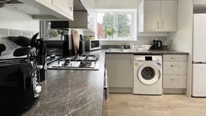 A modern kitchen with a gas stove, microwave, and built-in washing machine. - Worksop Newly Refurbished 2-bedroom House (Worksop)
