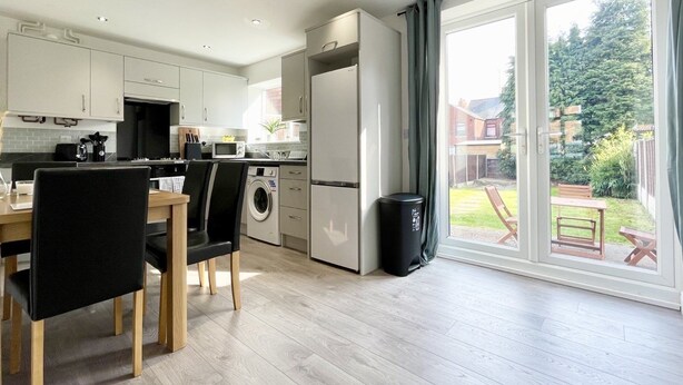 A modern kitchen with a dining area, a washing machine, and a large sliding glass door leading to a garden. - Worksop Newly Refurbished 2-bedroom House (Worksop)