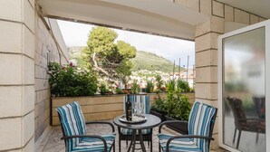 A patio with two striped chairs, a table with a bottle and glasses, and a view of a town and hills. - House Apartments Ariva (Dubrovnik)