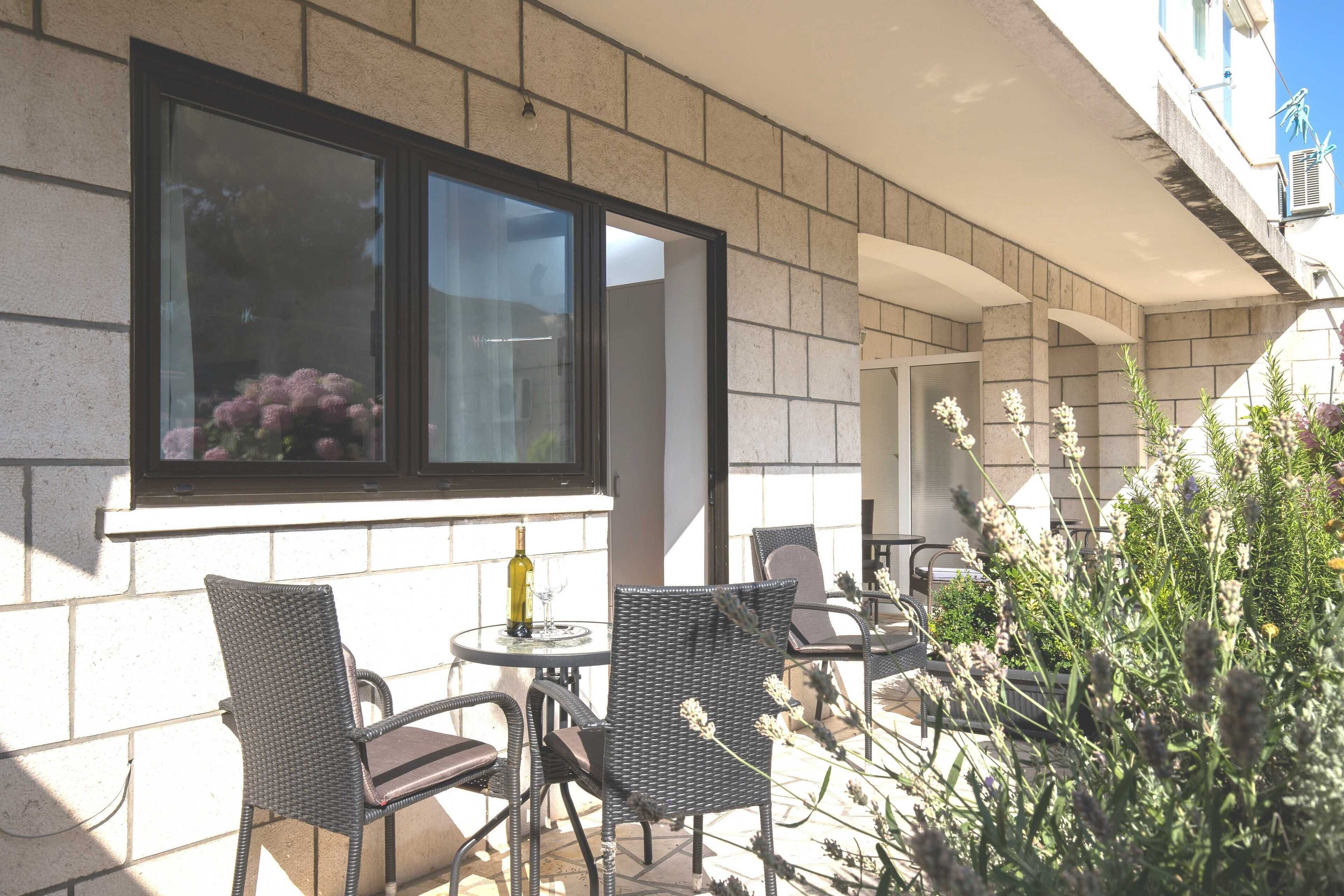 Une terrasse extérieure avec des meubles en osier, une table avec une bouteille et une fenêtre donnant sur un jardin.