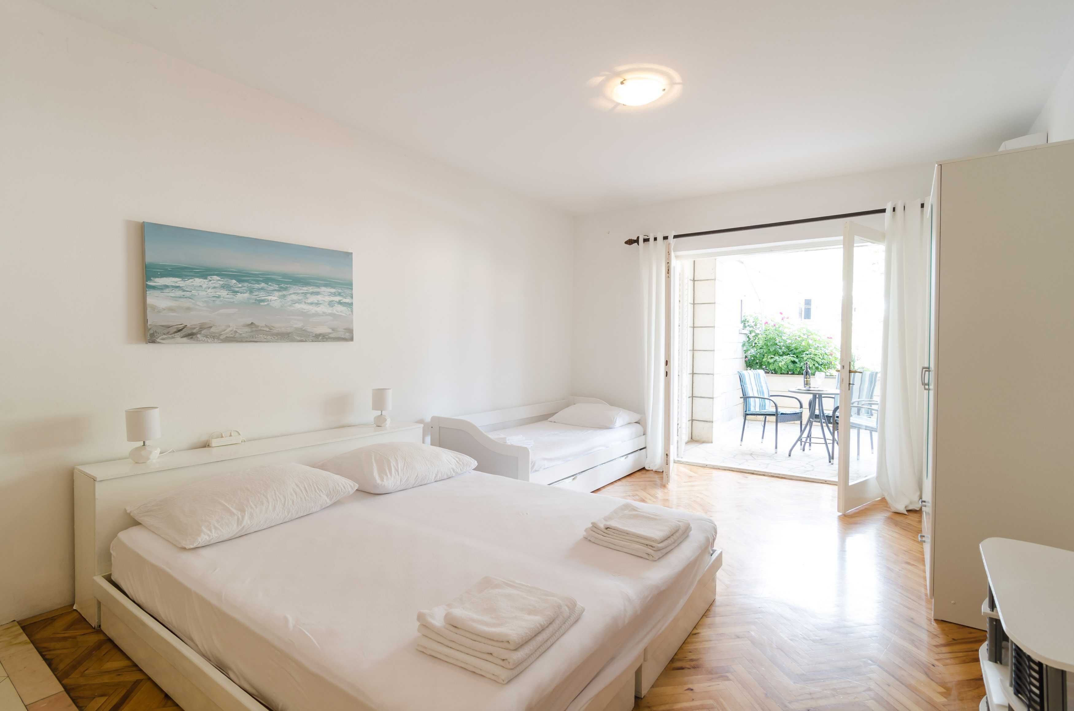 Ein Schlafzimmer mit einem Bett, einem zusätzlichen Bett, einem Gemälde, einem Tisch und einem Stuhl im Freien.