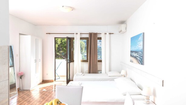 A hotel room with two beds, a desk, a chair, a laptop, and a window with curtains. - House Apartments Ariva (Dubrovnik)