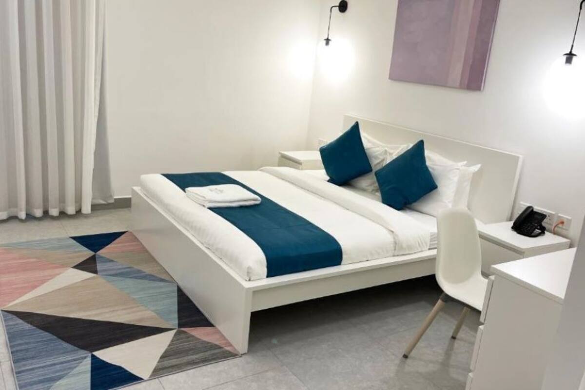 A modern hotel room with a bed, bedside table, chair, and a desk.