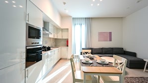 A modern kitchen with built-in appliances, a dining area with a table and chairs, and a living area with a sofa. - Terminal Inn By Edar City Center (Doha)