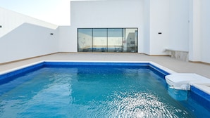 A swimming pool with a clear blue water, surrounded by white walls and a glass door leading to a covered area. - Terminal Inn By Edar City Center (Doha)
