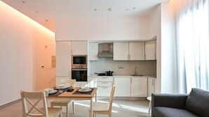 A modern kitchen with white cabinets, a microwave, and a stove. There is a dining area with a table and chairs. - Terminal Inn By Edar City Center (Doha)