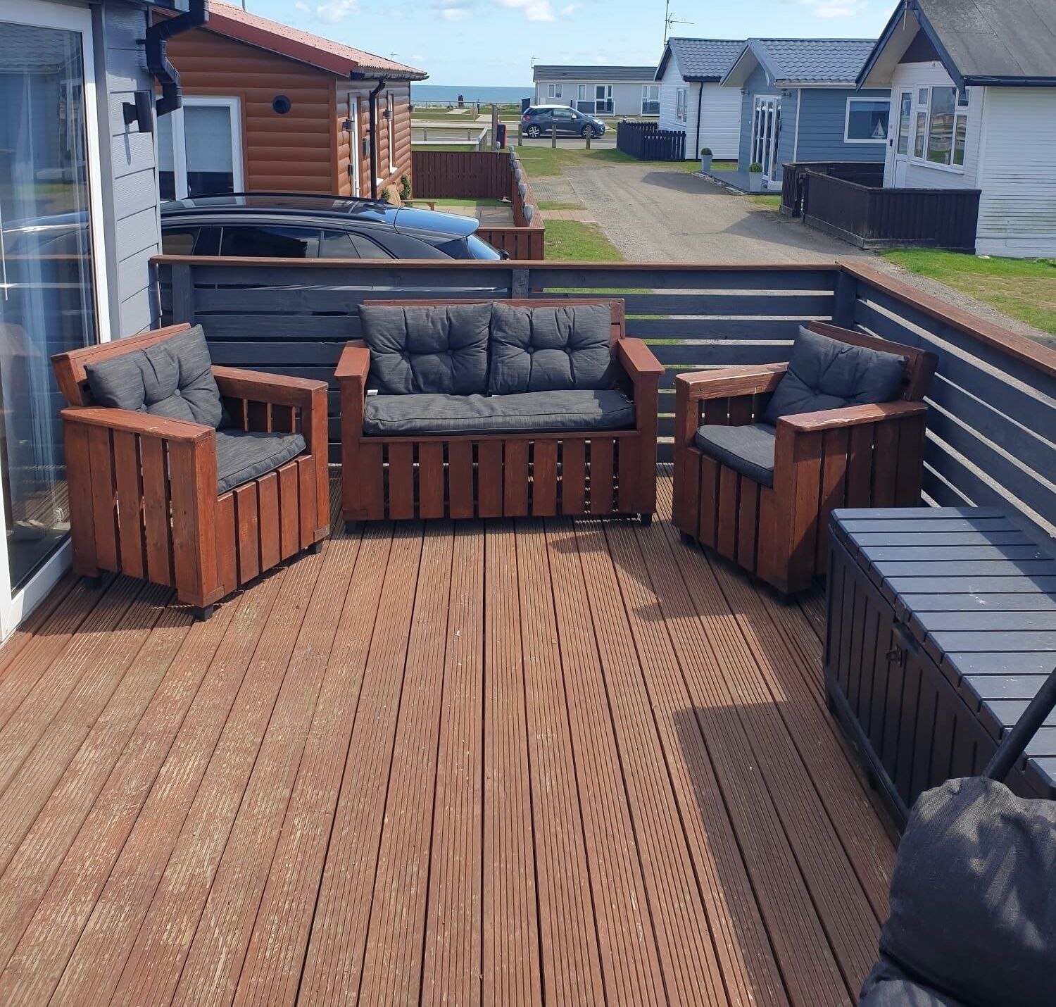 A wooden deck with a sofa and chairs, a glass door, and a view of a road and buildings.