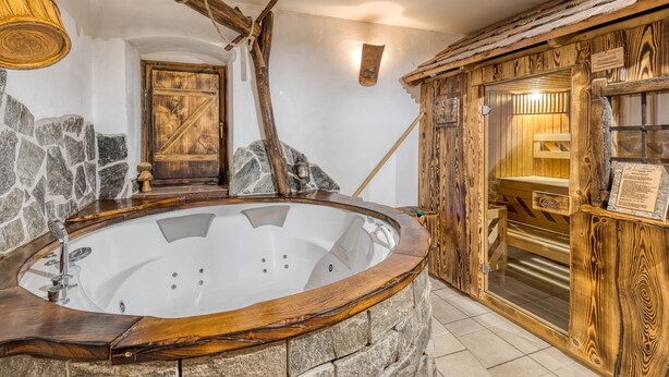 A stone-walled bathroom with a wooden bathtub, a rustic wooden door, and a stone wall.