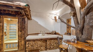 A rustic wooden room with a bed, a wooden bench, and a tree trunk.