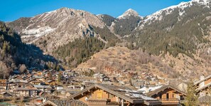 A mountain village with wooden buildings, a ski lift, and snow-capped mountains in the background.