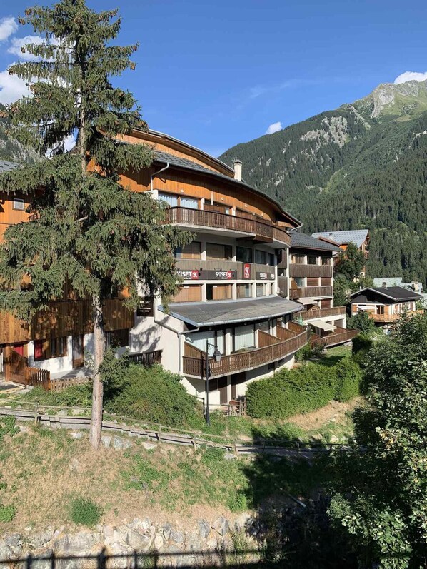 A multi-story hotel with wooden balconies, set against a mountainous backdrop.