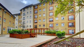 Un edificio residencial de varios pisos con balcones, un patio con bancos y jardineras.