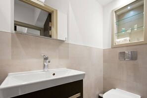 Une salle de bain moderne avec un lavabo blanc, un meuble sombre et une étagère en verre où sont rangés les articles de toilette.