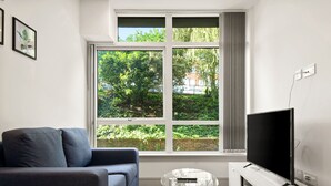 A modern living room with a grey sofa, a glass coffee table, and a flat-screen TV on a white stand. - Charming 1-bed Apartment in Harrow (Harrow)