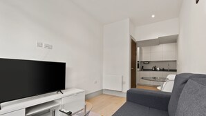 A modern living room with a flat-screen TV, grey sofa, and a glass coffee table. - Charming 1-bed Apartment in Harrow (Harrow)