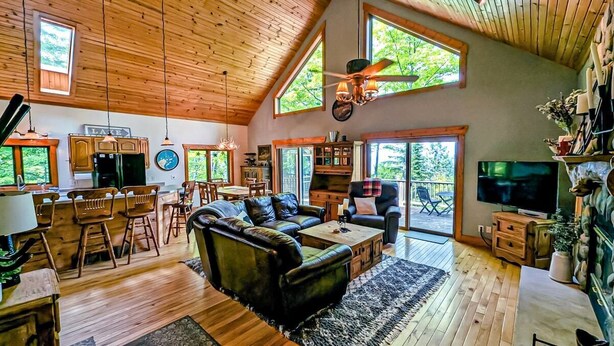 A spacious living area with a large sofa, dining table, and chairs, wooden floors, and a ceiling fan.