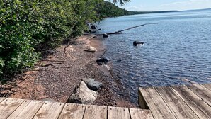 A wooden dock extending into a calm lake with a rocky shoreline and dense greenery on one side.