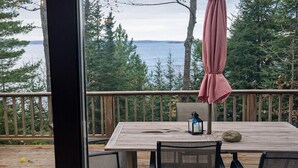 A wooden deck with a table and chairs, a pink umbrella, and a view of the water and trees.
