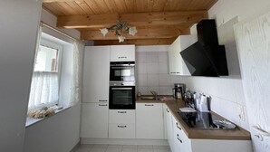 A compact kitchen with white cabinets, a wooden ceiling, and a window with curtains. - 2 Bedroom Apartment in Kempten (Kempten)