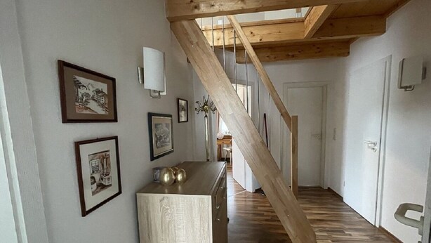 A hallway with wooden flooring, a staircase with a wooden beam, and framed pictures on the walls. - 2 Bedroom Apartment in Kempten (Kempten)