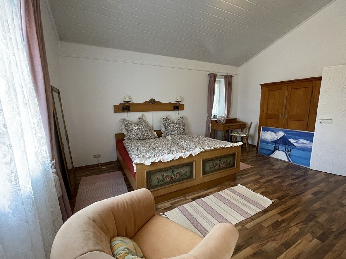 Une chambre à coucher avec un lit en bois, une chaise, un tableau et une armoire en bois.