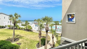 A balcony with a view of the ocean, palm trees, and a building with a stained glass window. - Summer & July 4th Savings at Beachside Colony Tybee's ONLY Oceanfront Resort 2/2 (Tybee Island)
