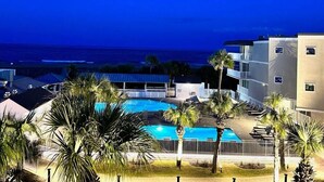 A swimming pool with palm trees, a view of the ocean, and a building with balconies. - Summer & July 4th Savings at Beachside Colony Tybee's ONLY Oceanfront Resort 2/2 (Tybee Island)
